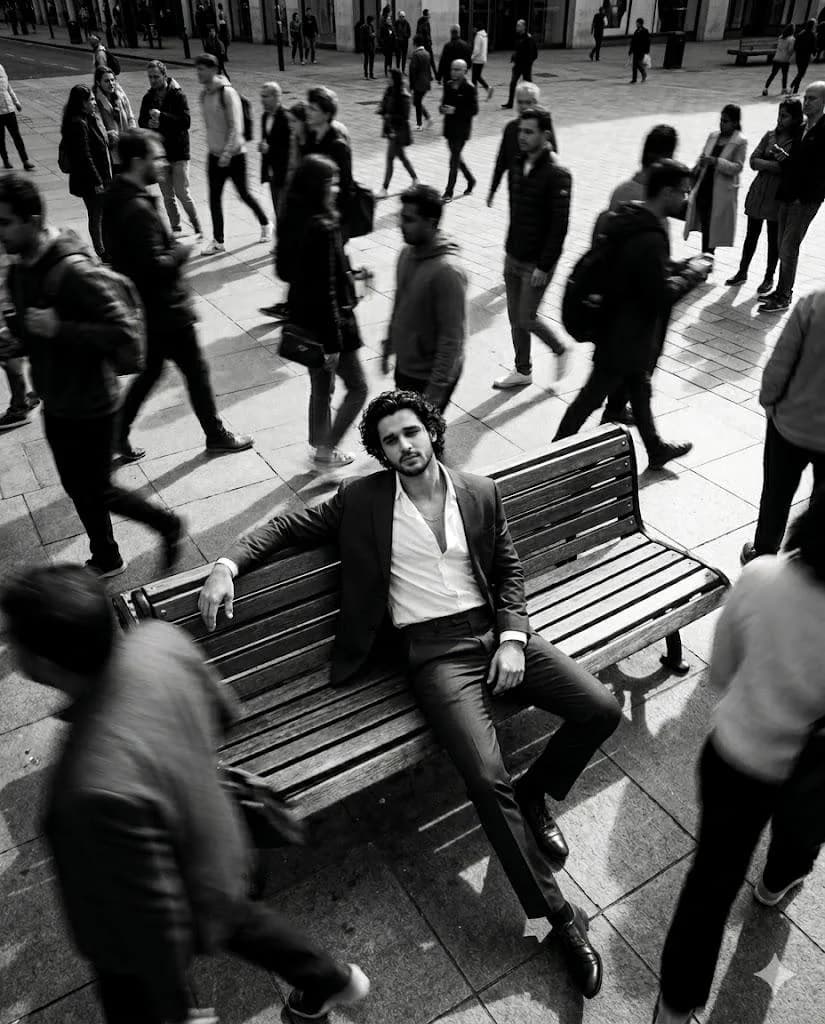High-angle black and white cinematic portrait of suited man on bench with motion-blurred crowd
